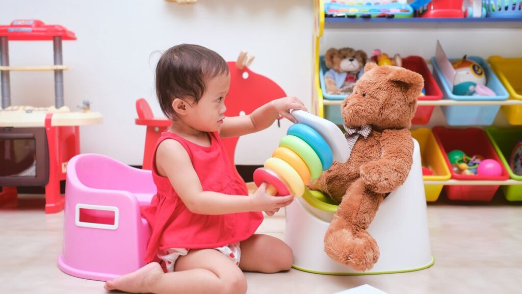 Toddler plays with her teddy bear on a training potty