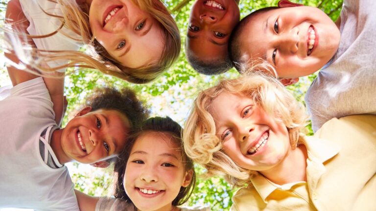 Happy kids heads-together under trees, representing the levels of autism support needs across the spectrum