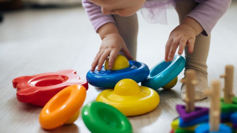 Toddler reaching for colorful toys during play, to illustrate the topic about age for ABA therapy